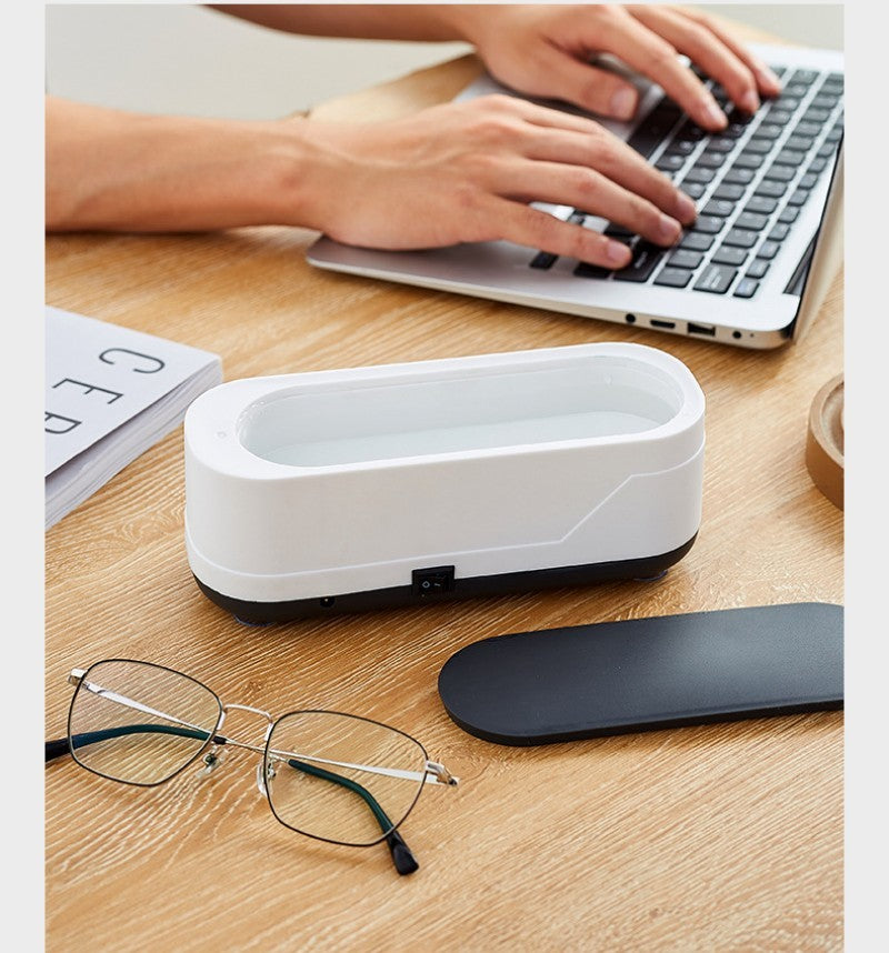 Multifunctional white and black sterilization box open on a wooden desk, shown beside eyeglasses, a laptop, and a book—ideal for cleaning everyday items like glasses, utensils, and small gadgets.