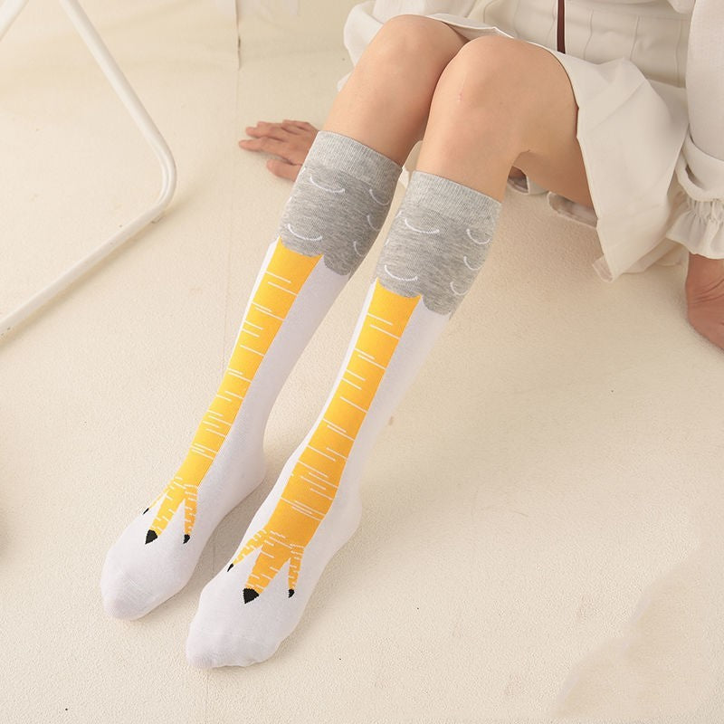 Person sitting on a light-colored floor wearing a white skirt and a pair of novelty white knee-high socks designed to resemble yellow bird legs with grey feather tops and claw-like toe designs.