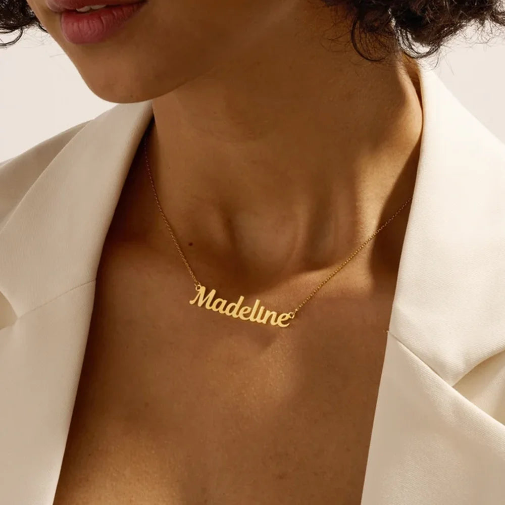 Gold necklace with 'Madeline' pendant on a person wearing a beige blazer.