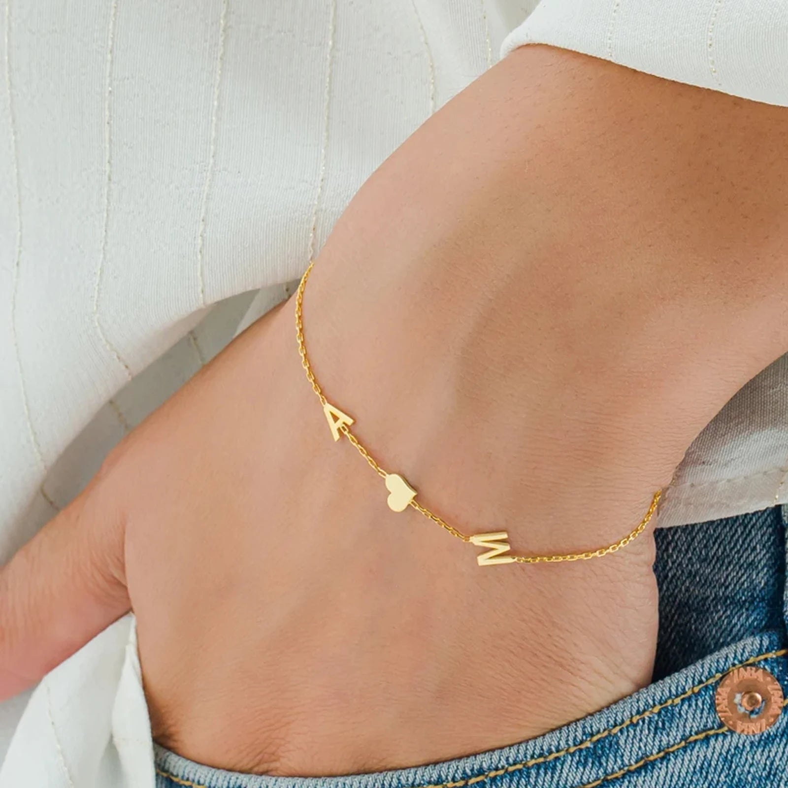 Gold bracelet with letter 'M' on a person's ankle against a neutral background