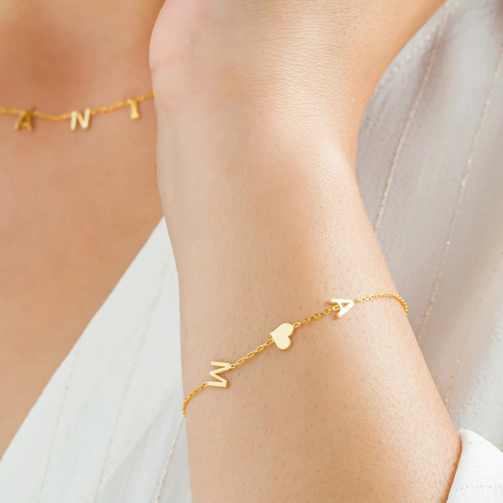 Gold bracelet with letter charms on a person's ankle against a neutral background