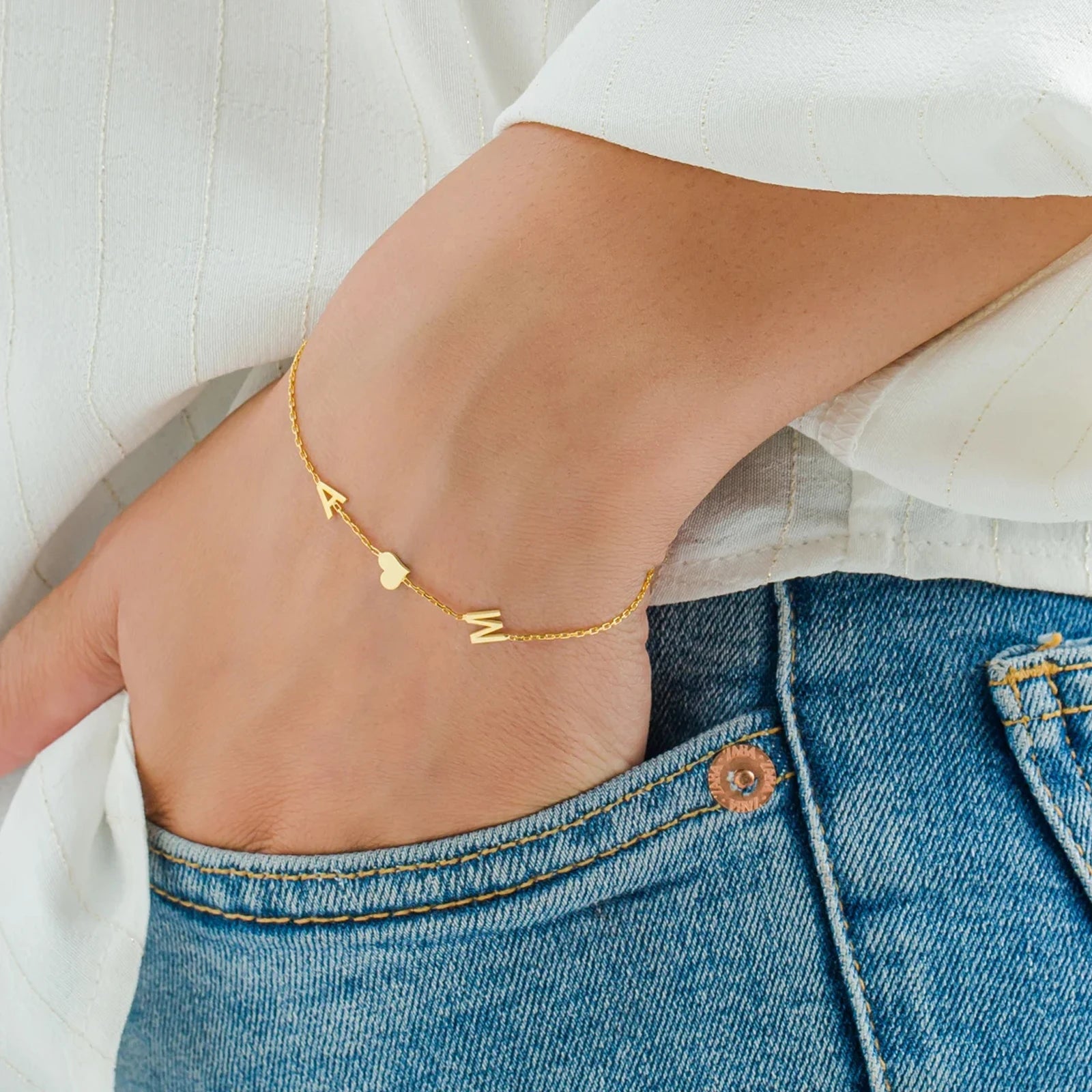 Gold bracelet with letter charms on a person's ankle against a white background