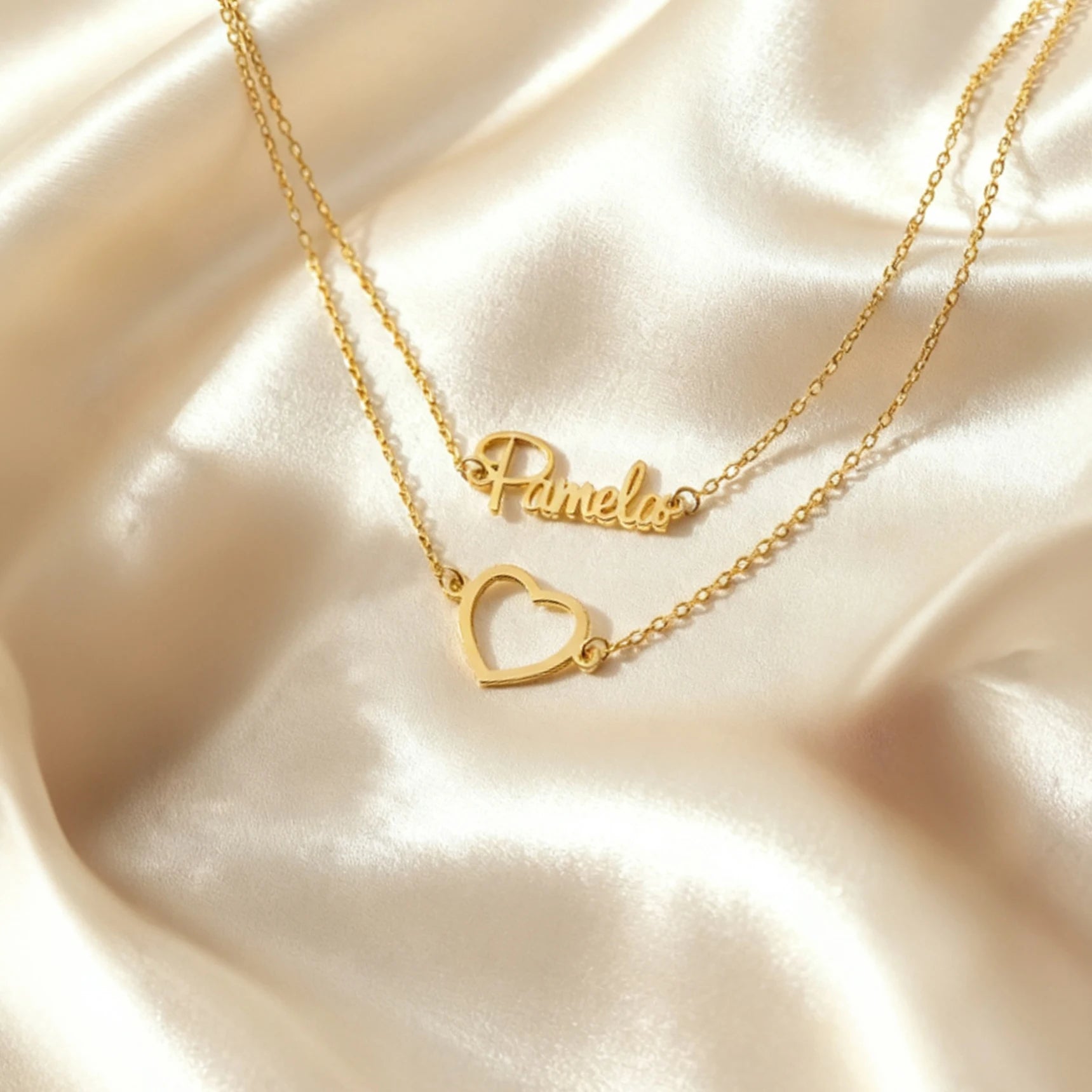 Gold necklace with a heart-shaped pendant and 'Pamela' inscription on a beige fabric background
