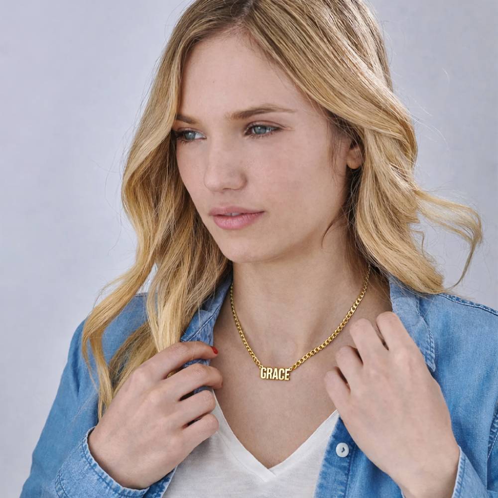 Woman wearing a gold necklace with 'GRACE' on it against a plain background