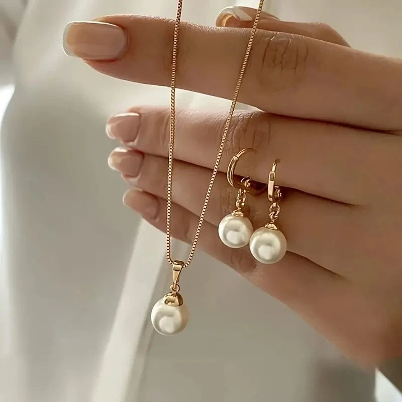 Hand holding a gold necklace with pearl pendants against a neutral background