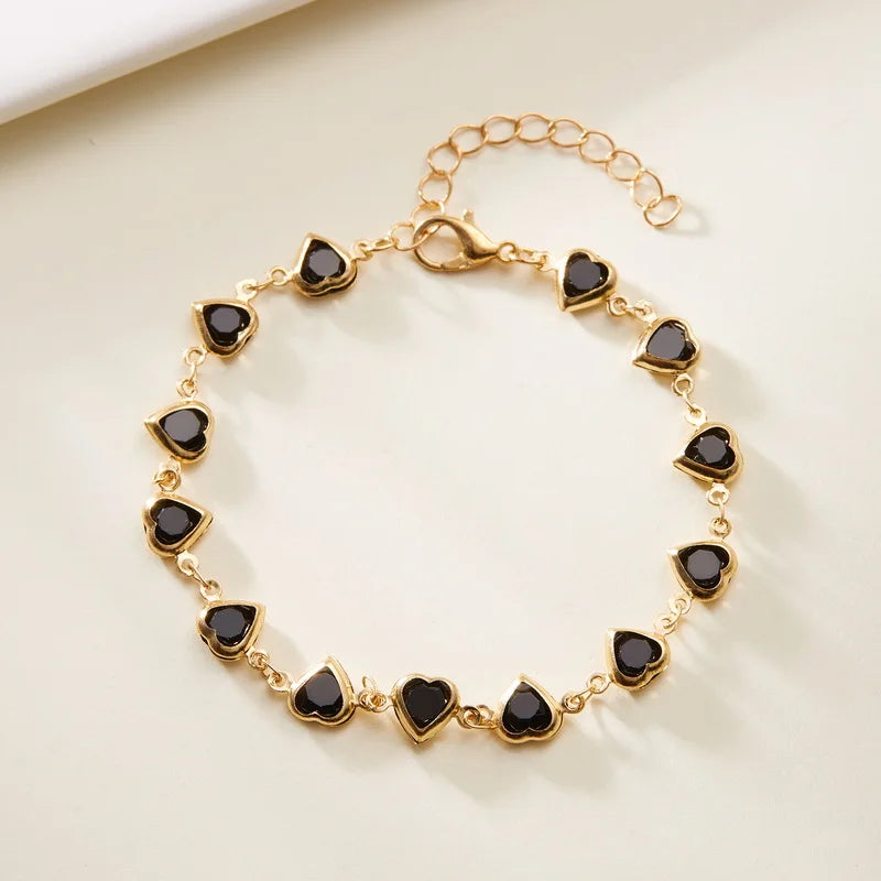 Gold bracelet with black heart-shaped stones on a beige background
