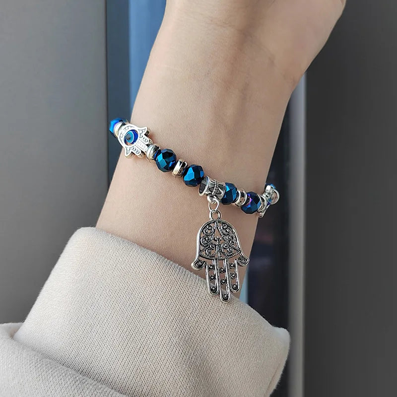 Bracelet with blue beads and silver hamsa charm on a wrist against a neutral background
