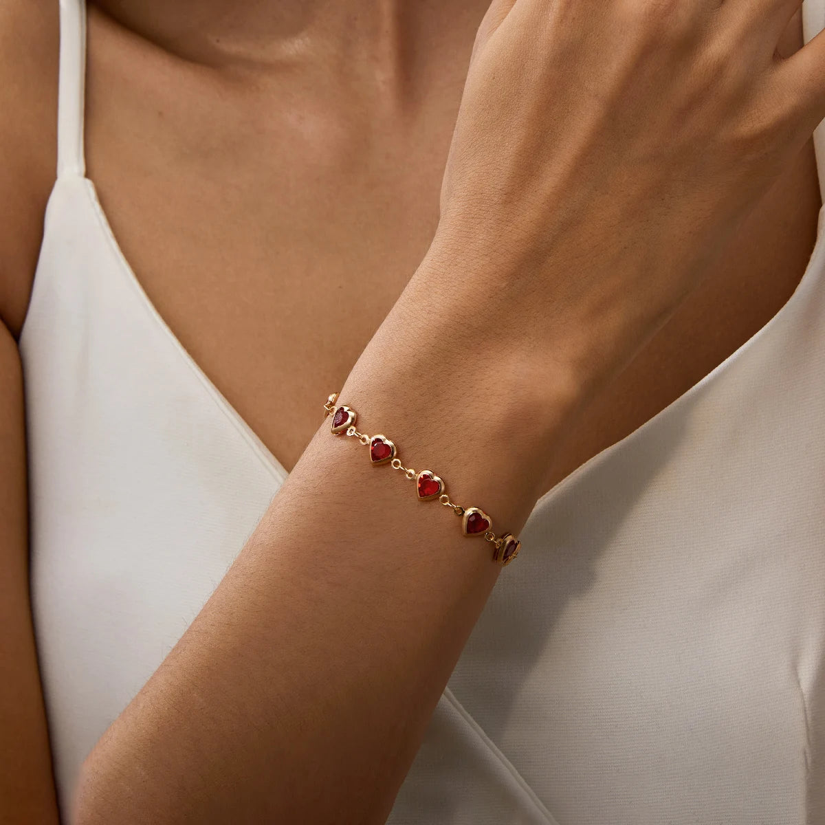 Gold bracelet with red gemstones on a person's wrist against a neutral background