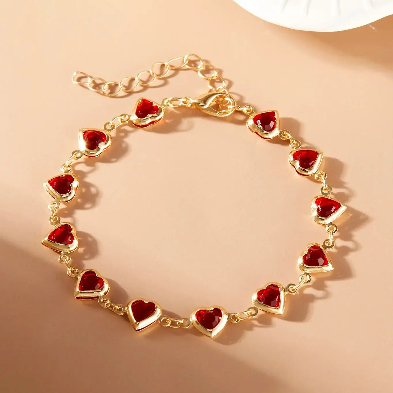Gold bracelet with red heart charms on a beige background