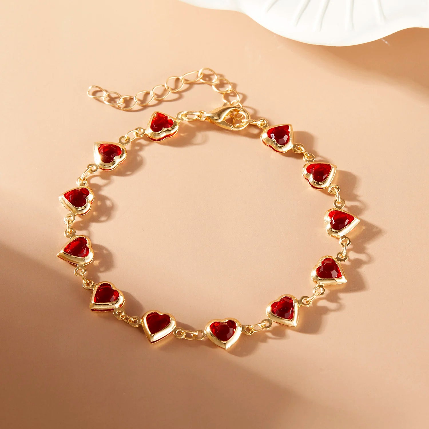 Gold bracelet with red heart charms on a beige background