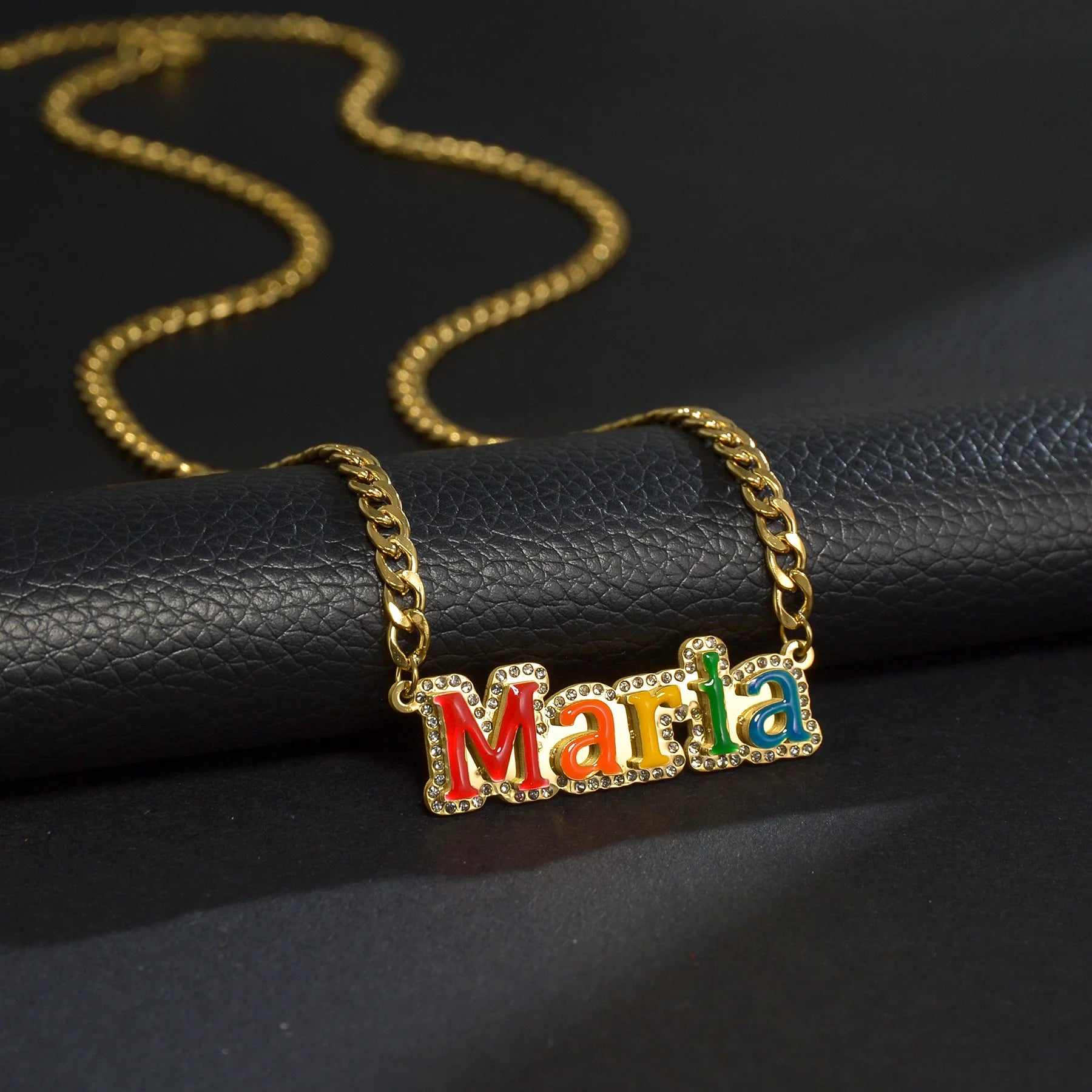 Gold necklace with colorful 'Maria' pendant on a black surface