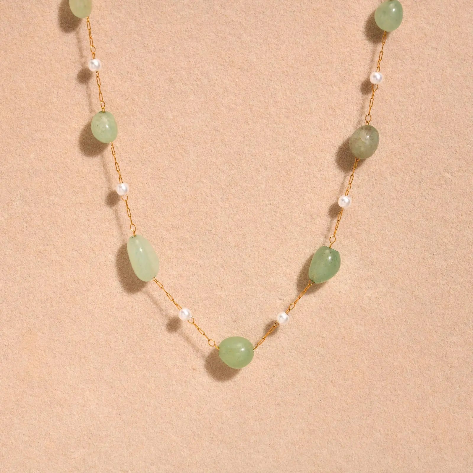 Necklace with green beads and gold chain on a beige background