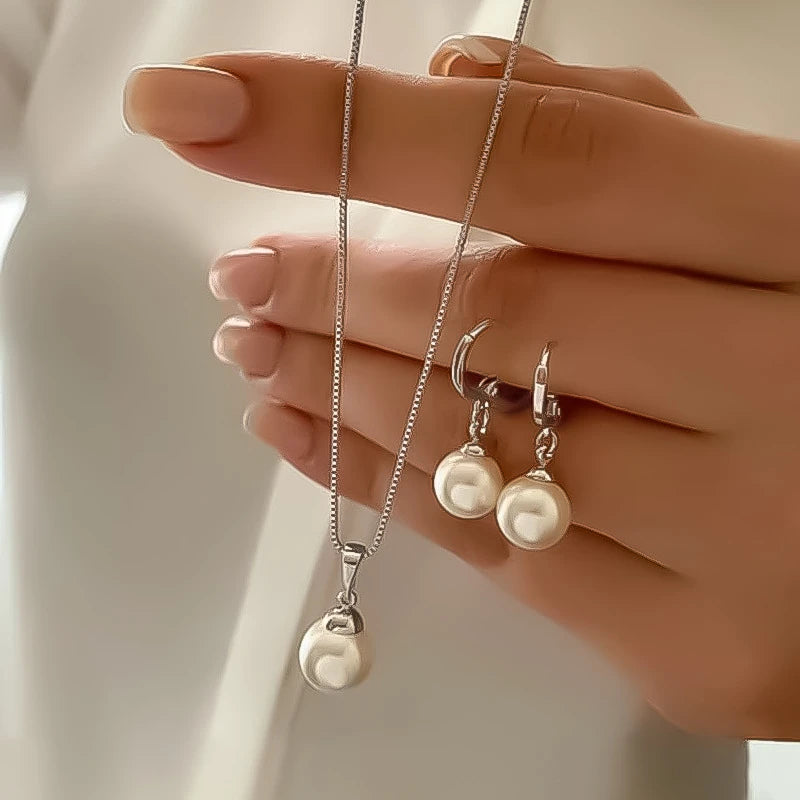 Pearl necklace and earrings held by a hand against a neutral background