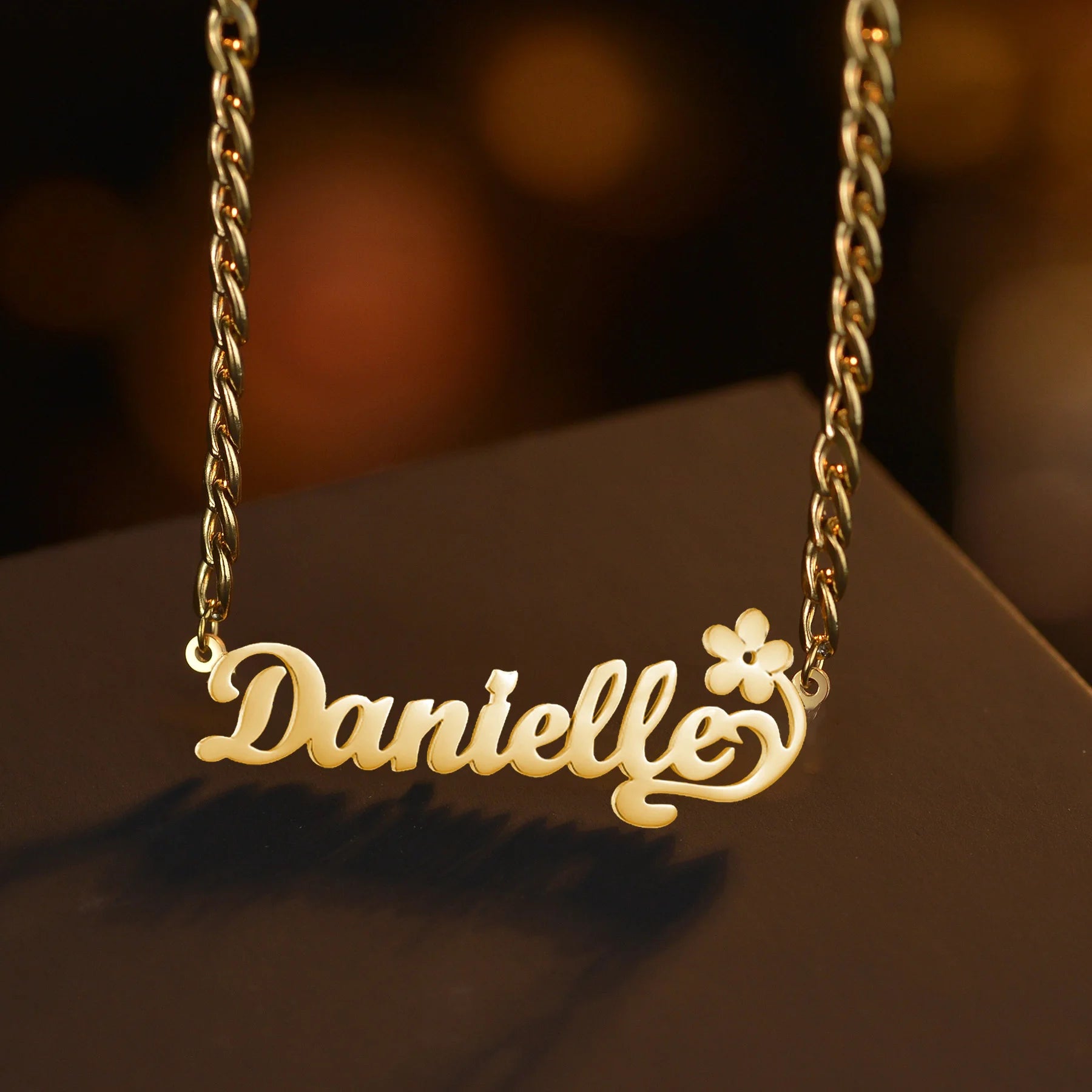 Gold necklace with 'Danielle' and a flower design on a dark background