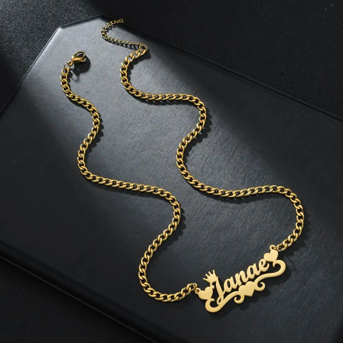 Gold chain necklace with 'Elena' pendant on a dark surface