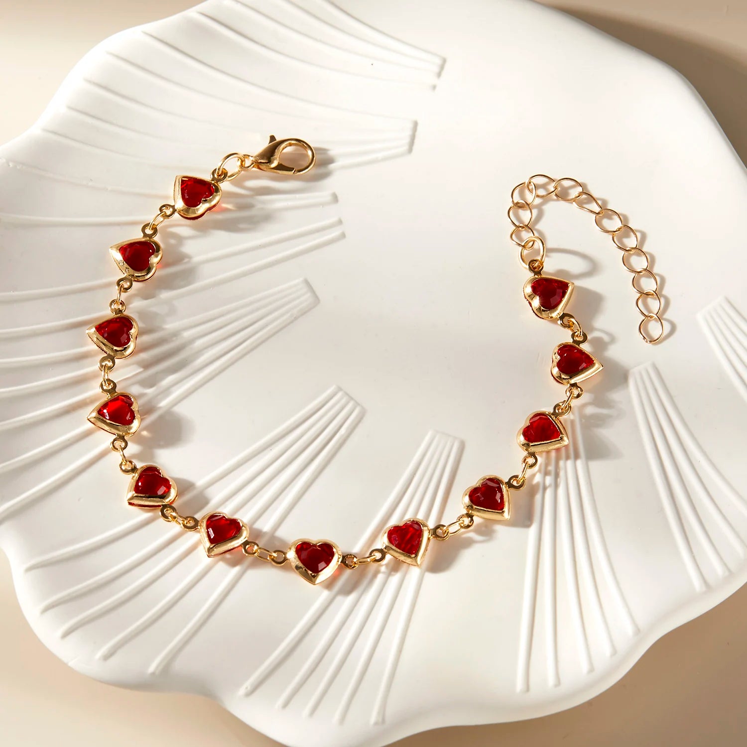 Gold bracelet with red heart charms on a white textured surface