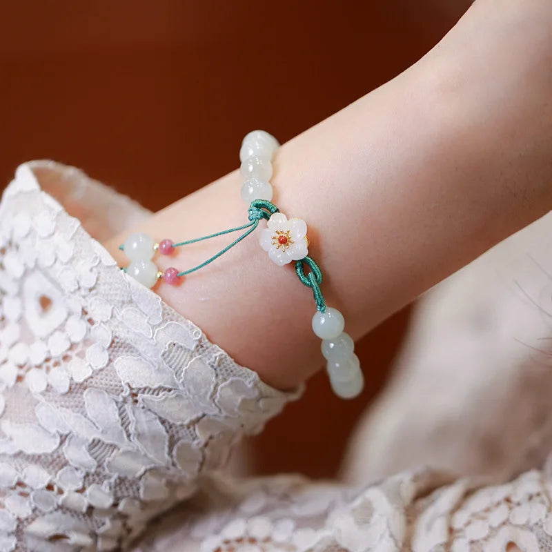 Close-up of a hand wearing a beaded bracelet with a floral charm, against a blurred background.