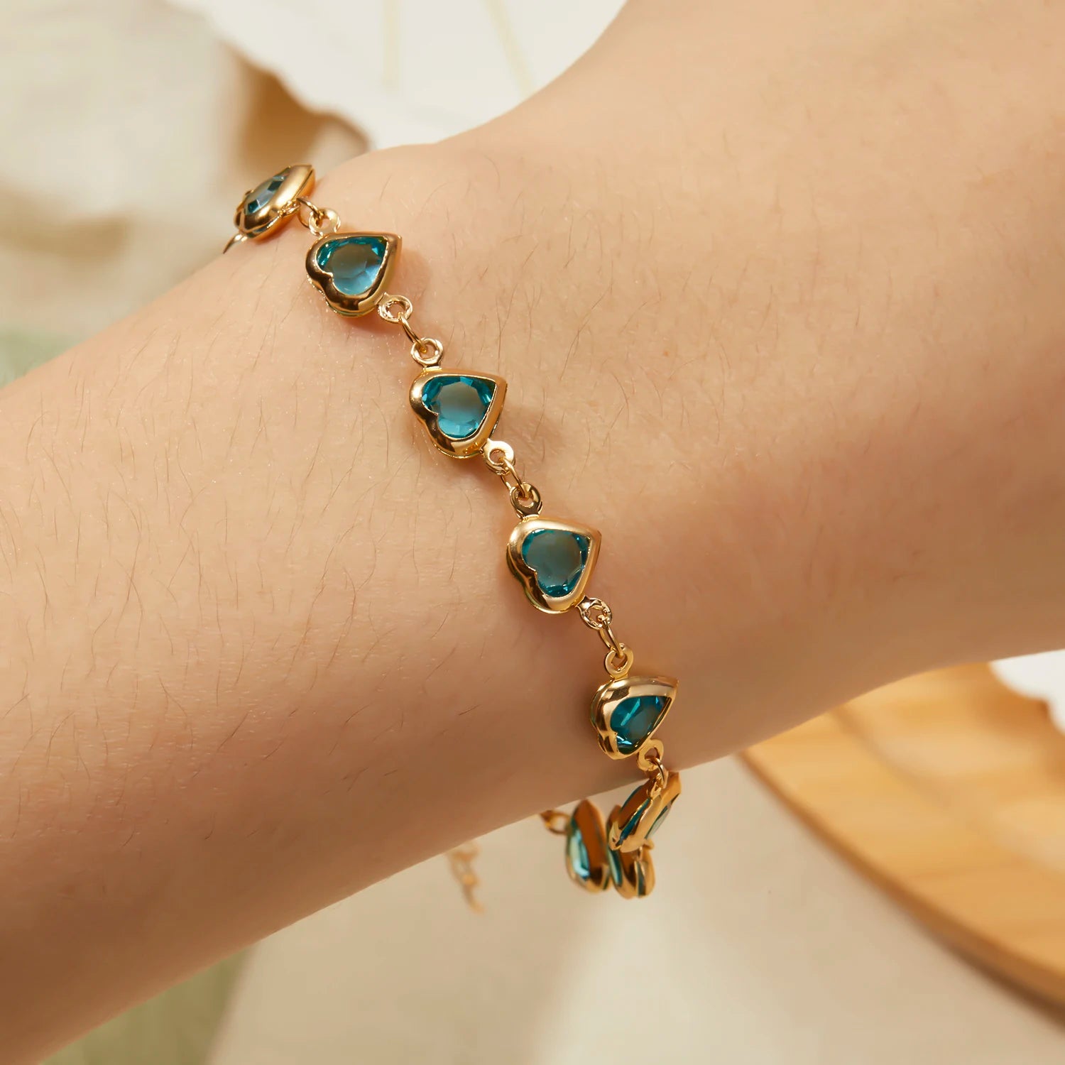 Gold bracelet with heart-shaped blue stones on a wrist against a neutral background