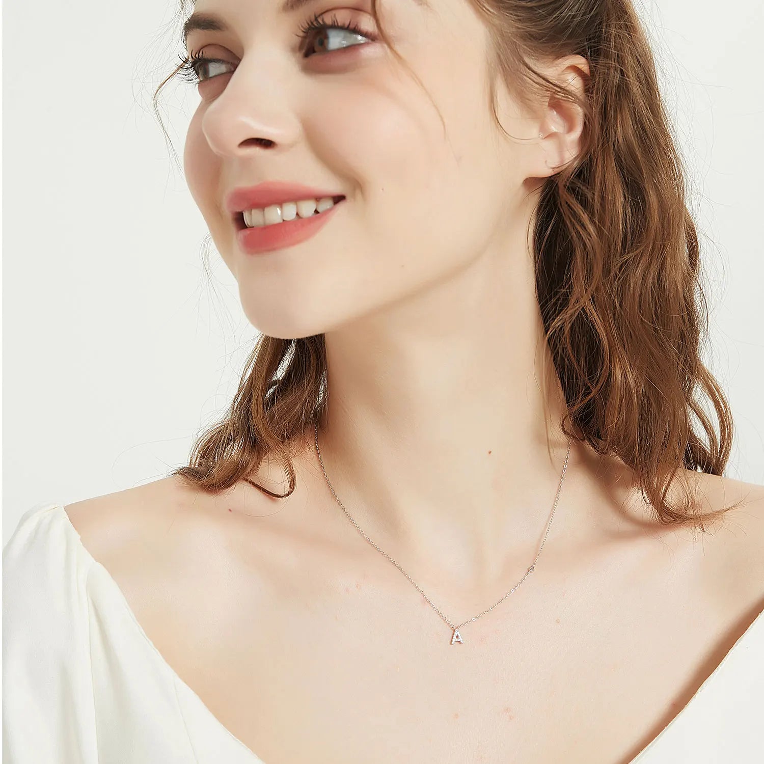 Woman wearing a delicate necklace with a small pendant on a plain background