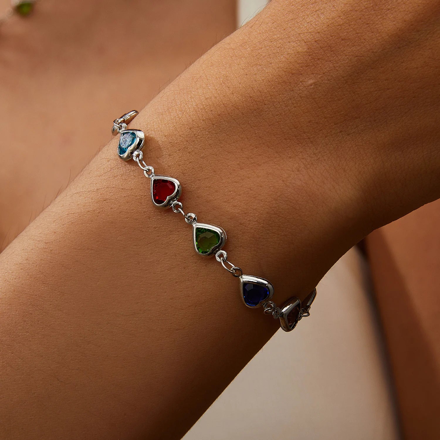 Bracelet with heart-shaped colorful stones on a wrist against a neutral background