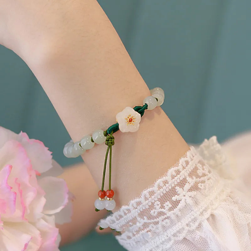 Hand wearing a bracelet with floral design and beads, against a blurred background