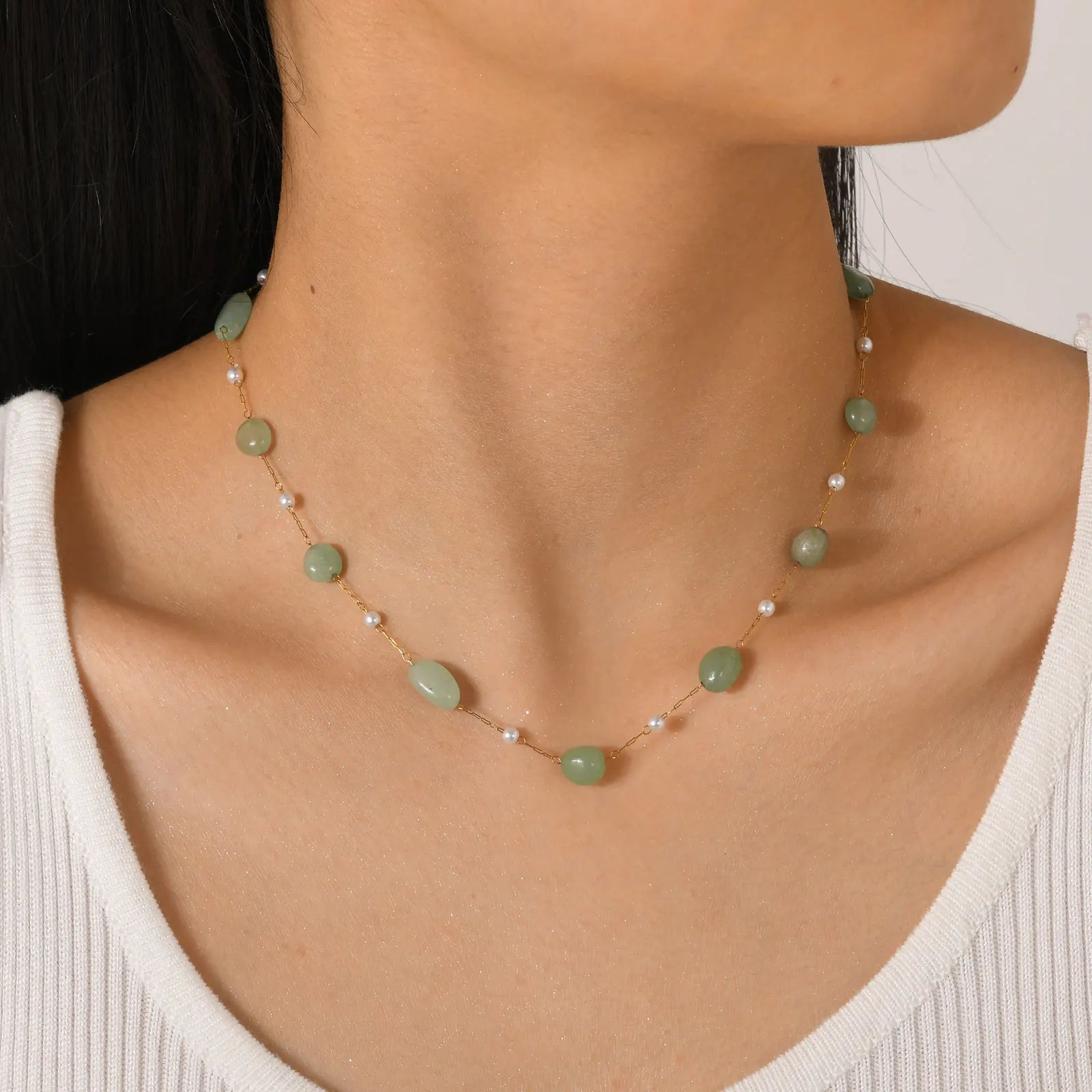 Necklace with green beads and white pearls on a person wearing a white top.