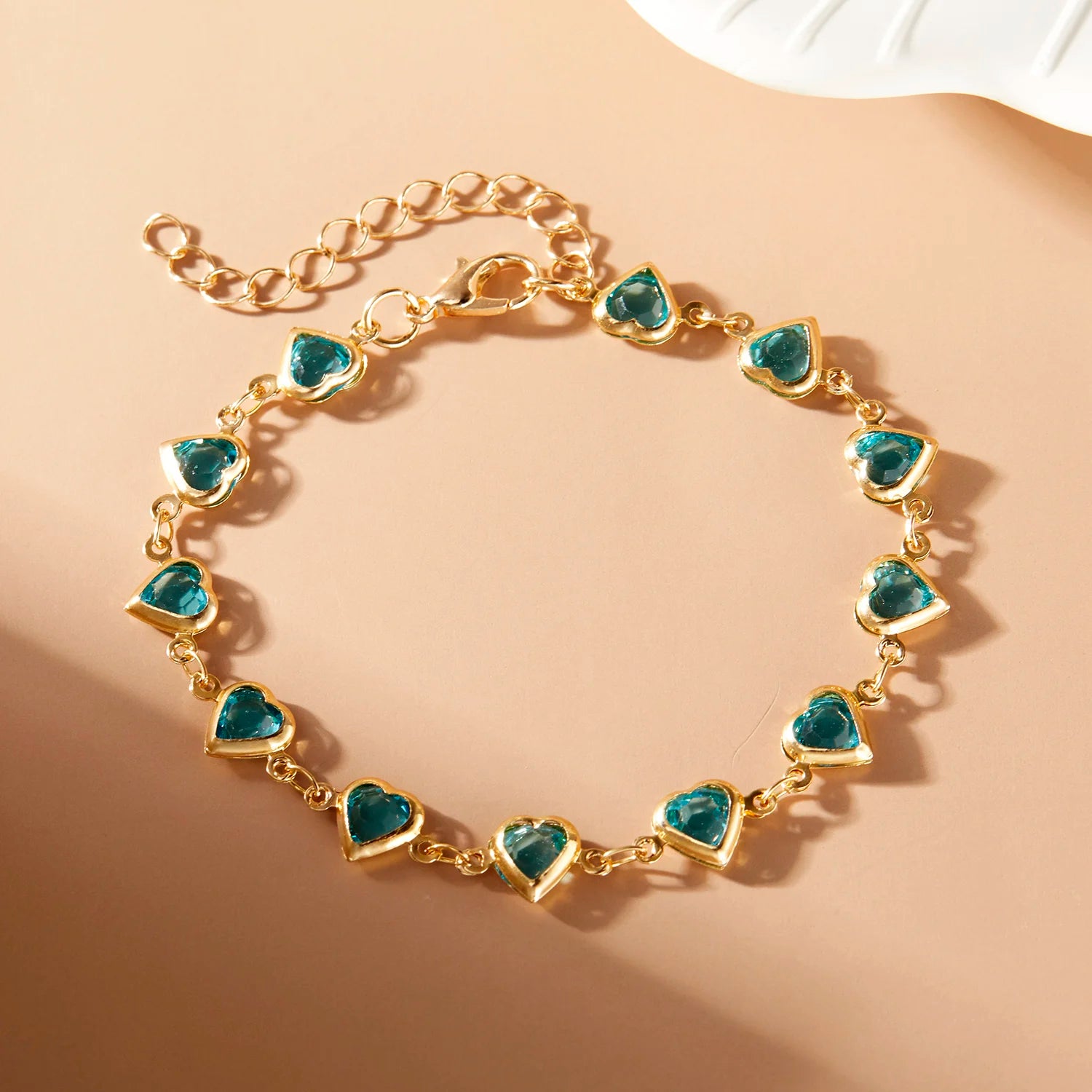 Gold bracelet with heart-shaped blue gemstones on a beige background