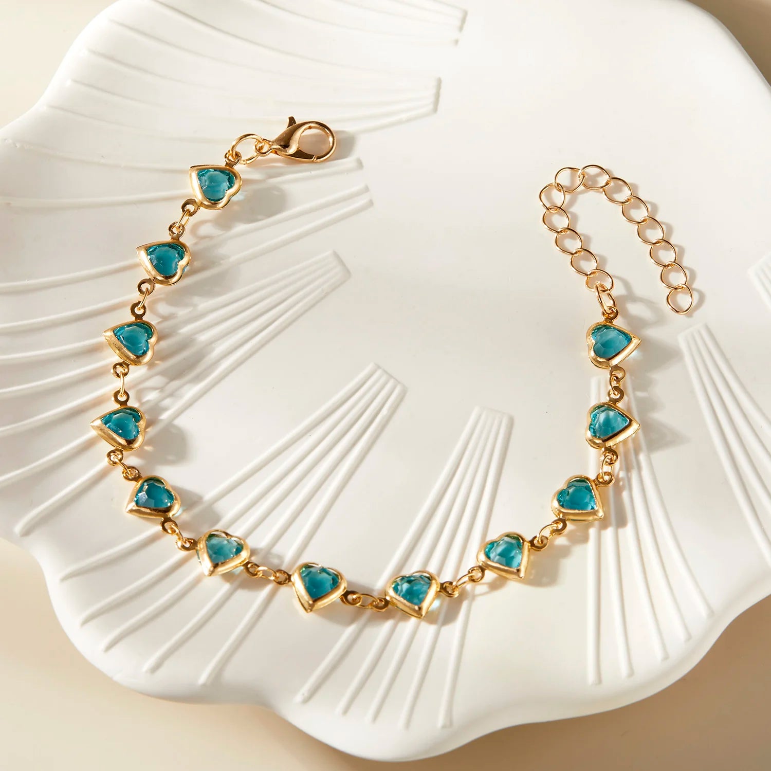 Gold bracelet with turquoise heart-shaped stones on a white shell