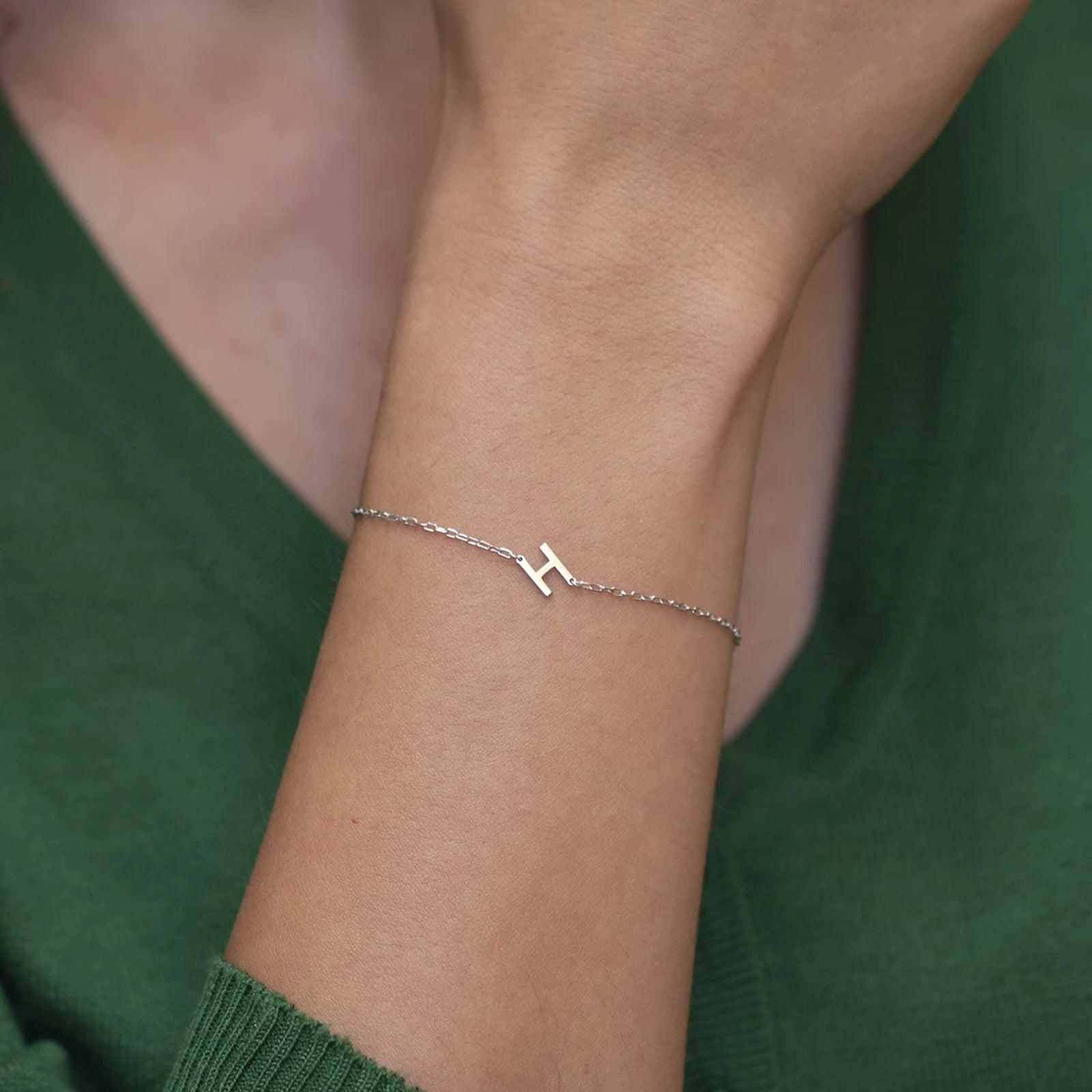Silver bracelet with a letter 'H' on a wrist against a green background