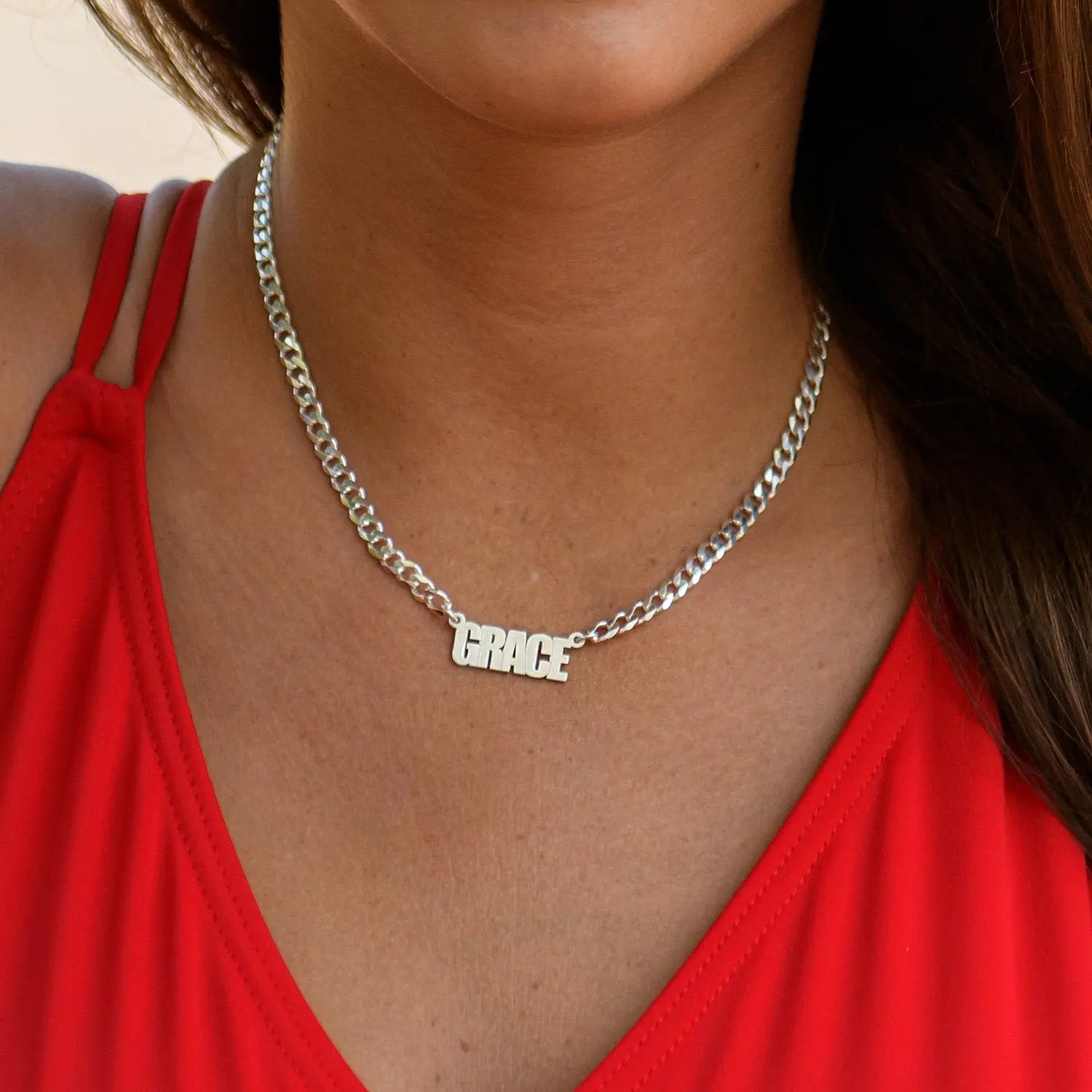 Silver necklace with 'GRACE' pendant worn by a person in a red top.
