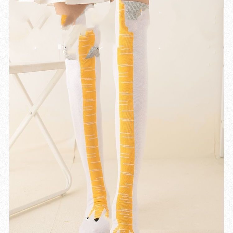 Model standing indoors wearing knee-high novelty socks designed to resemble yellow bird legs with grey feather tops and clawed feet on a white base.