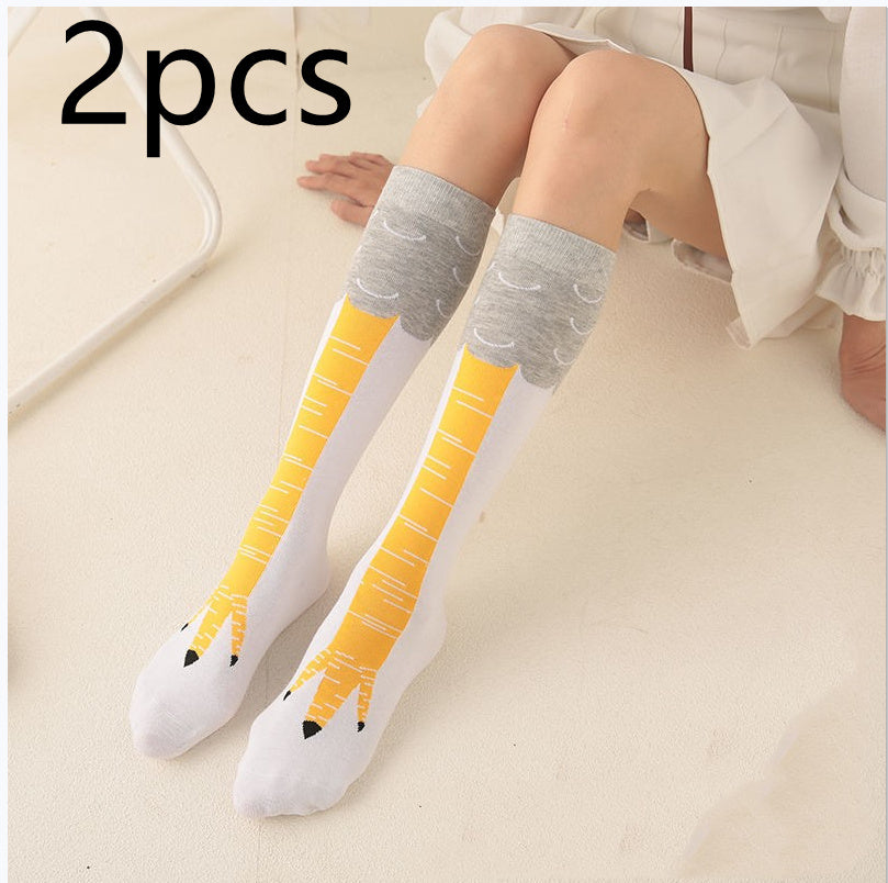 Person sitting on a light-colored floor wearing a white skirt and a pair of novelty white knee-high socks designed to resemble yellow bird legs with grey feather tops and claw-like toe designs; 