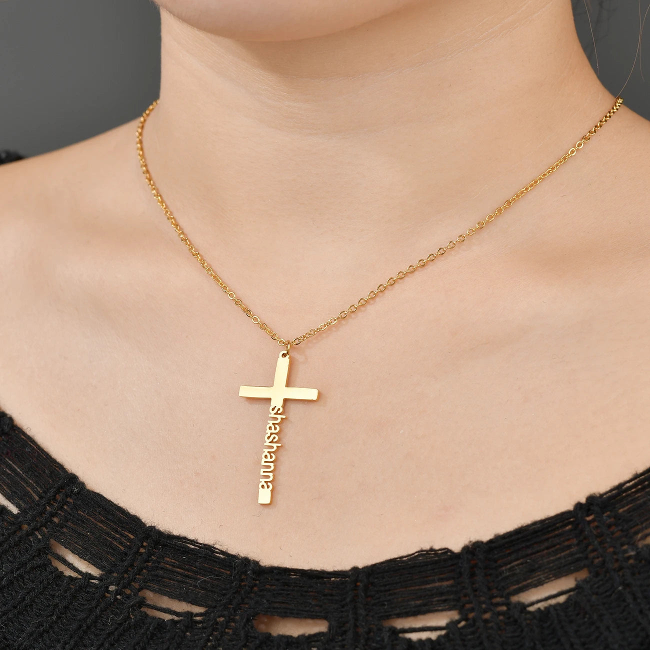 Gold cross necklace with engraved name on a person wearing a black top.