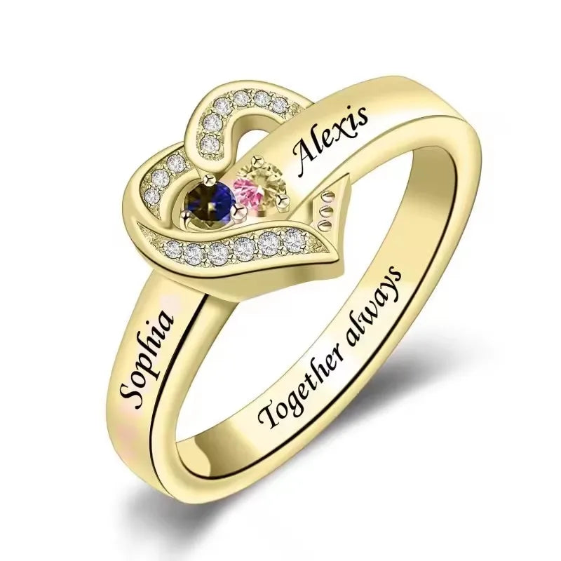 Gold heart-shaped ring with engraved names and gemstones on a white background
