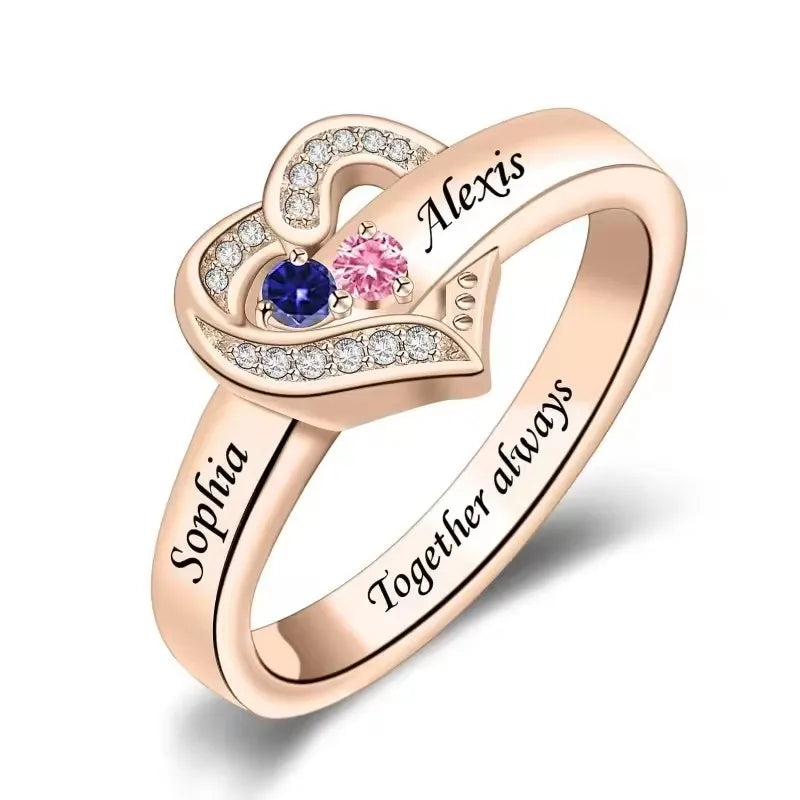 Rose gold heart-shaped ring with engraved names and colorful gemstones on a white background
