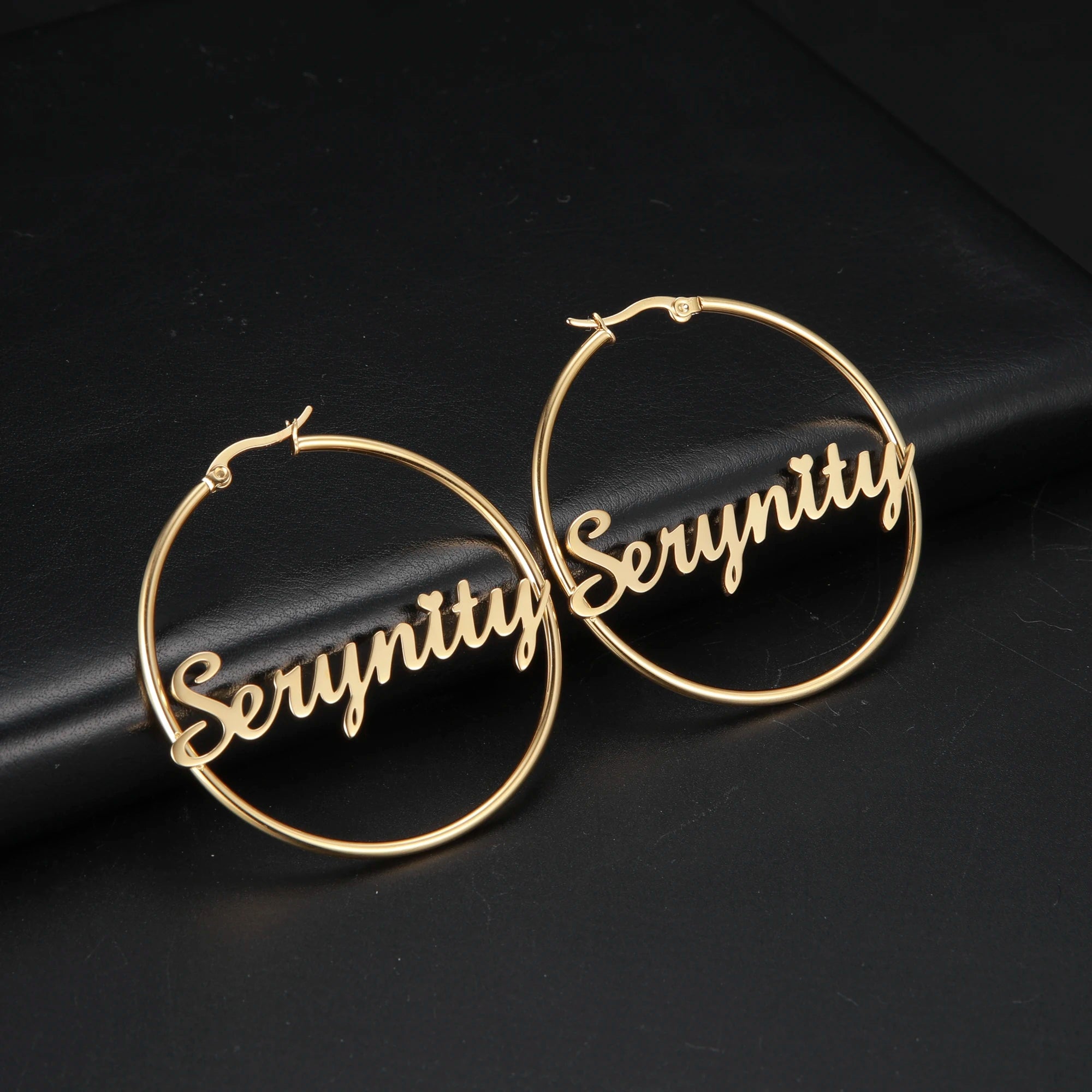 Gold hoop earrings with 'Serynity' engraving on a black background