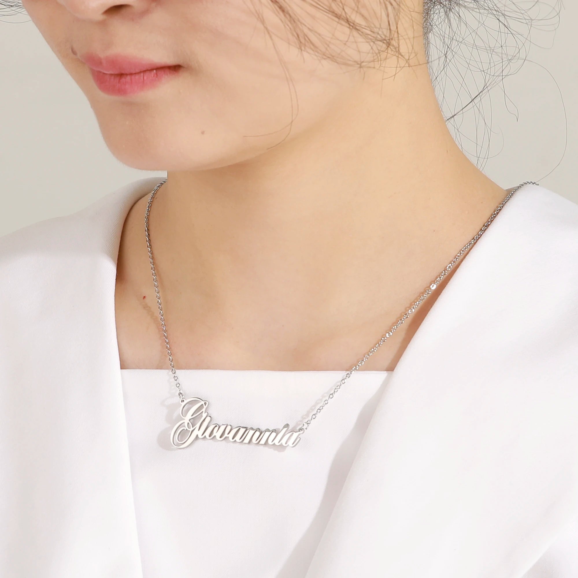 Silver name necklace worn by a person on a plain background