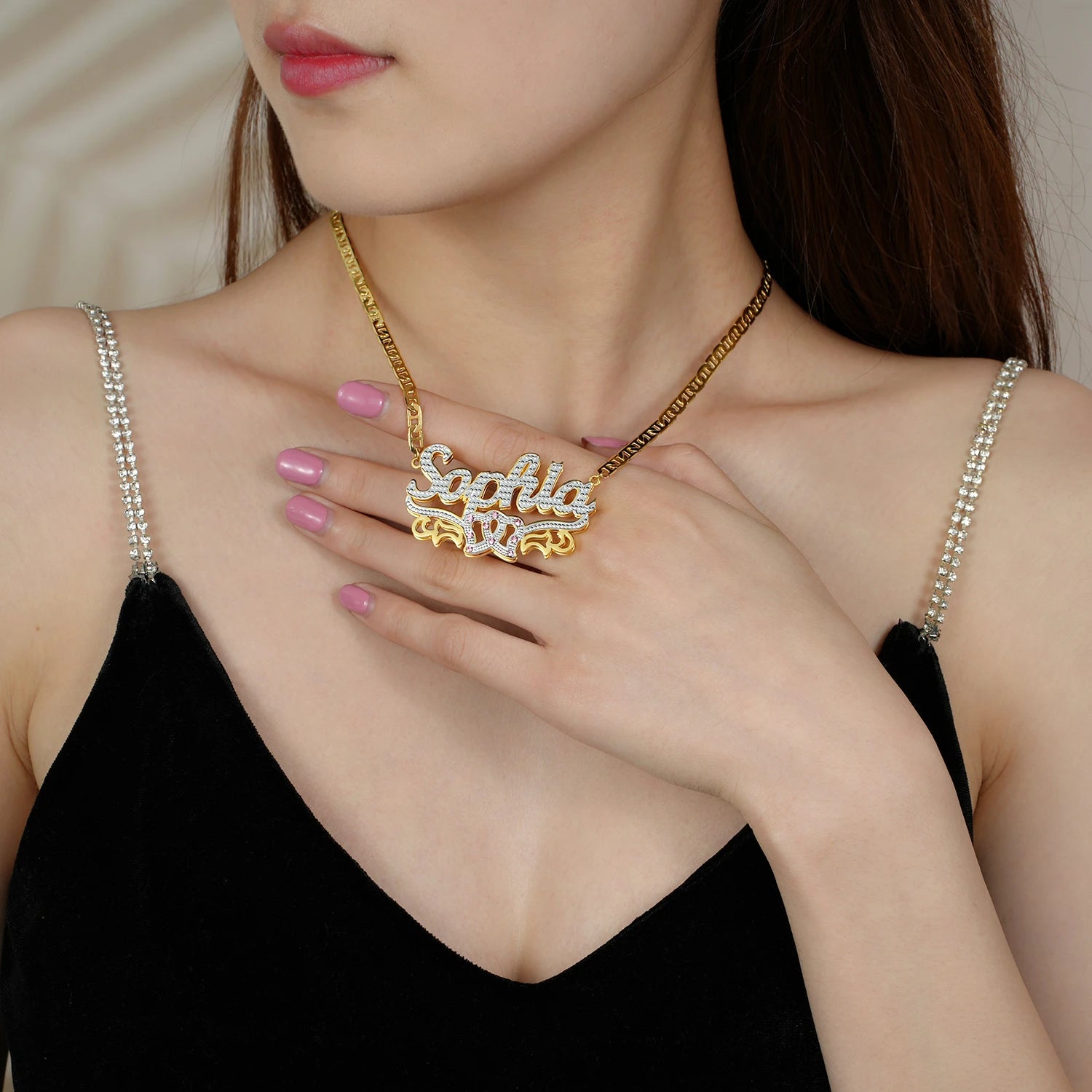 Woman wearing a gold necklace with a name pendant, holding it close to her chest.