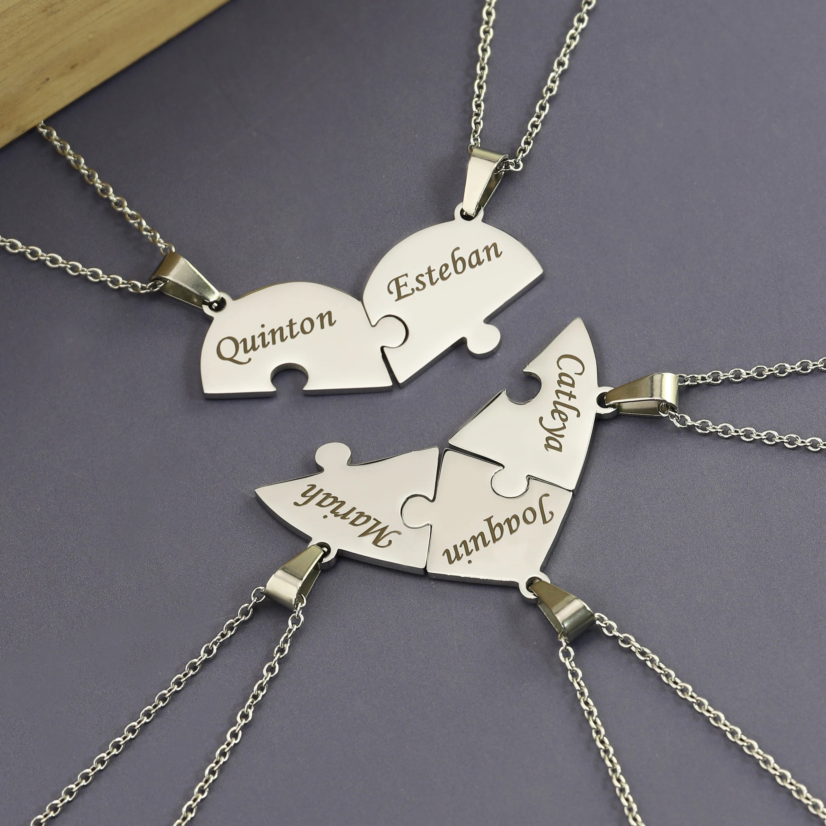 Silver puzzle piece necklaces with engraved names on a dark gray background