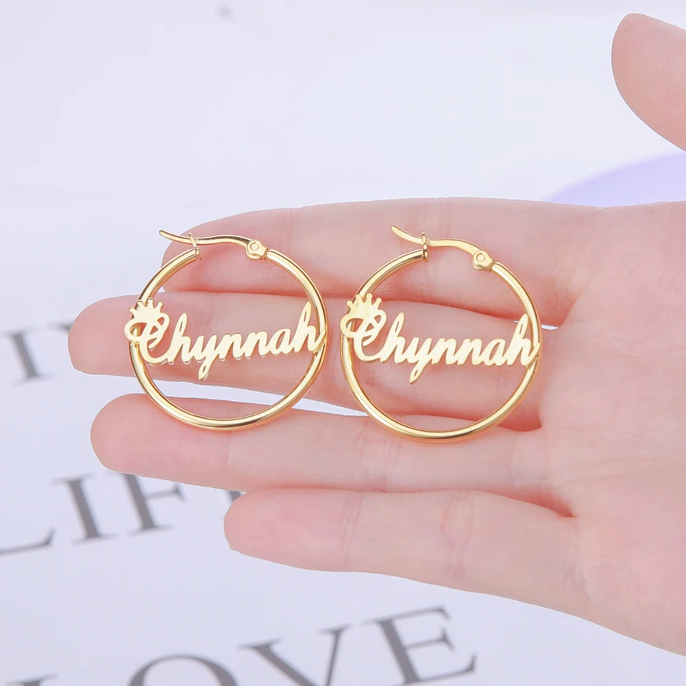 Gold hoop earrings with 'Chynnah' engraving held by a hand on a light background