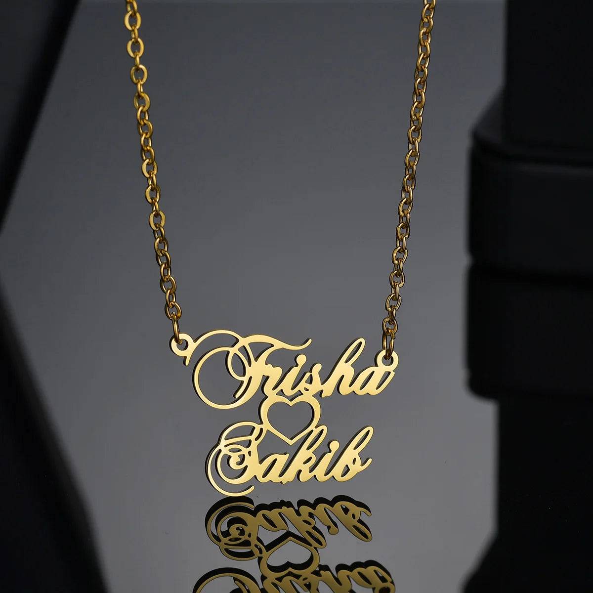 Gold necklace with 'Trisha & Sakib' engraving on a reflective surface
