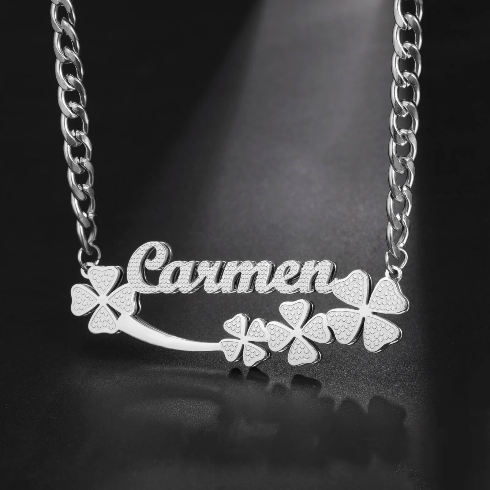 Silver necklace with 'Carmen' and clover designs on a dark background