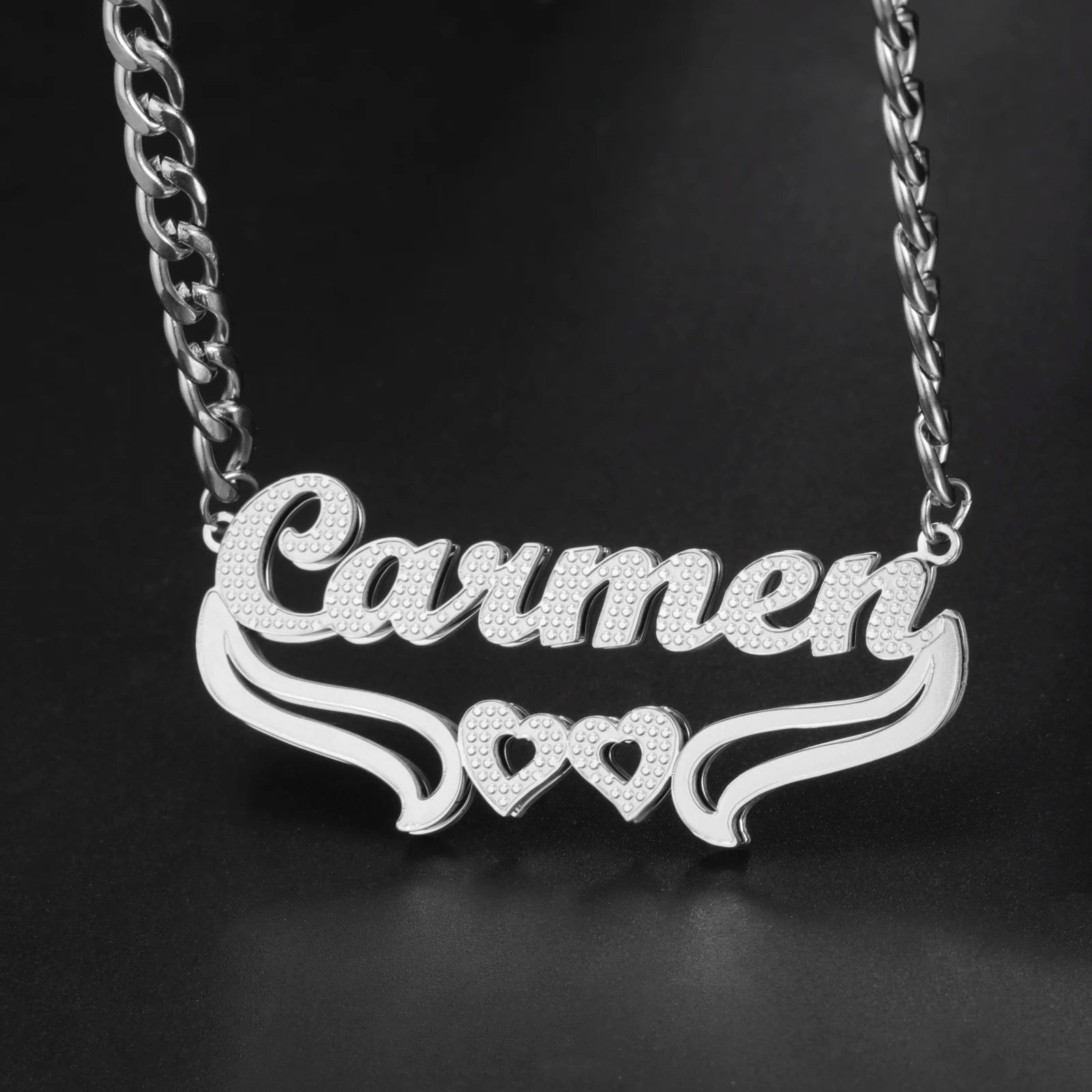 Silver necklace with 'Carmen' and heart designs on a black background