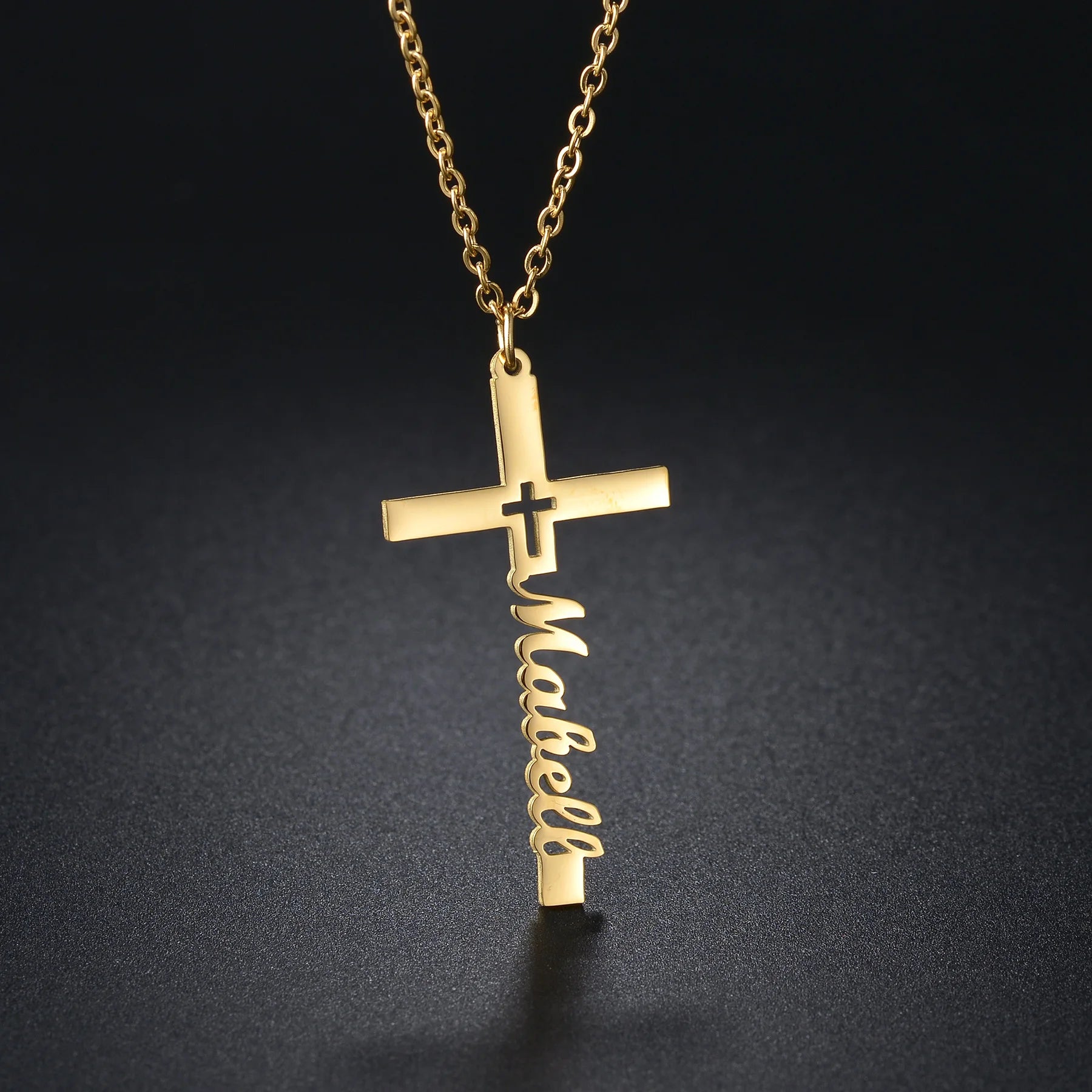 Gold cross necklace with 'Mabel' engraved on a dark background