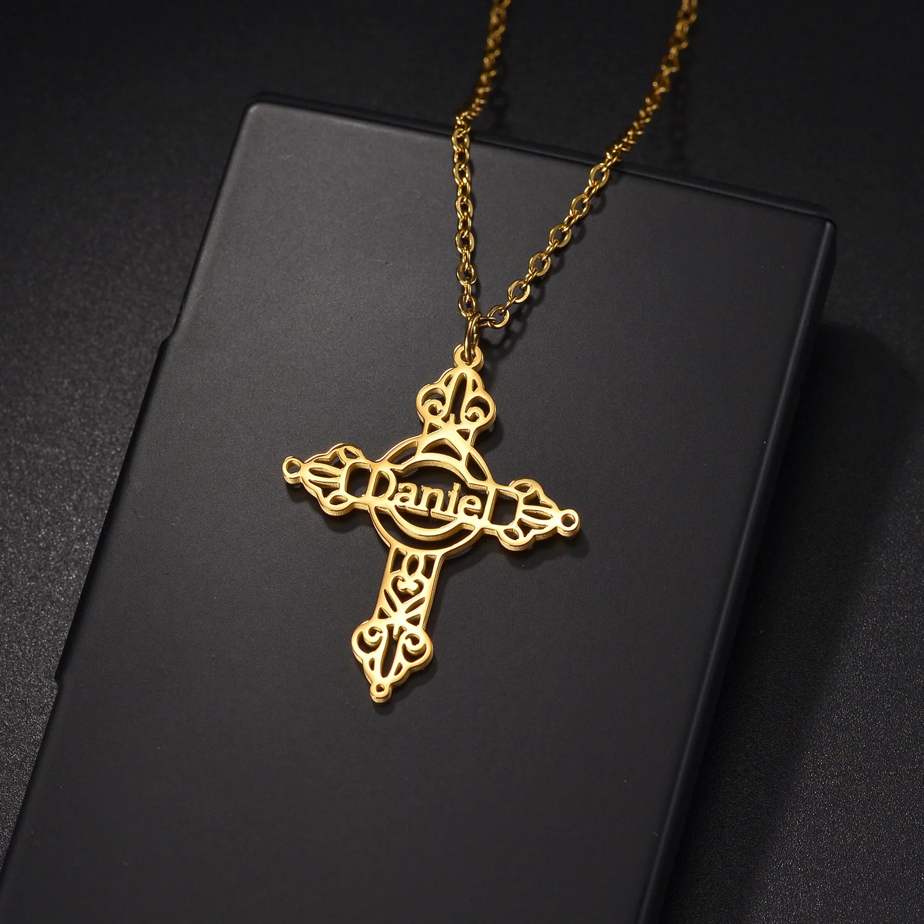 Gold cross necklace with 'Daniel' engraved on a black background