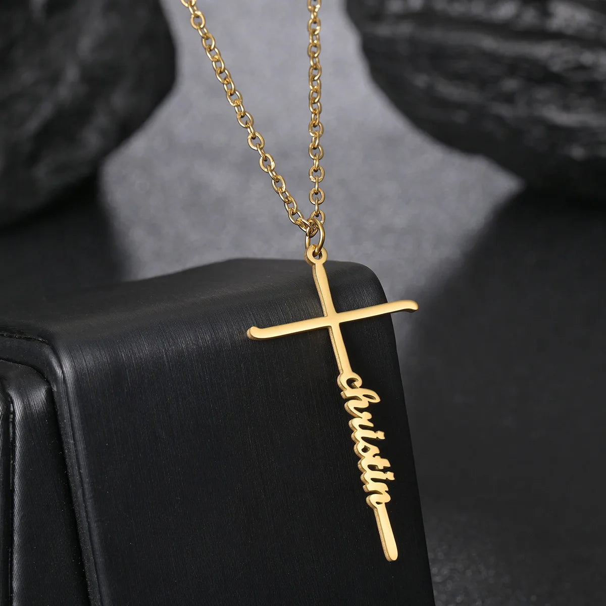 Gold cross necklace with 'Christian' engraving on a black surface