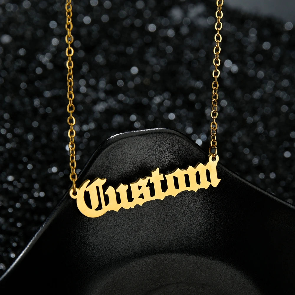 Gold 'Custom' necklace on a black stand with a dark, textured background