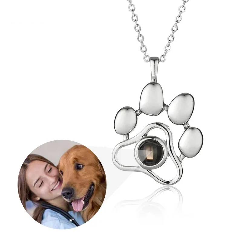 Silver paw-shaped pendant with a small round gemstone on a white background, next to a photo of a woman and her dog.