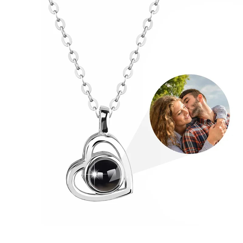 Silver heart-shaped pendant necklace with a black stone on a white background, featuring a circular inset of a couple embracing.