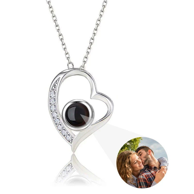 Heart-shaped necklace with a black gemstone and diamonds, featuring a photo of a couple on a card.